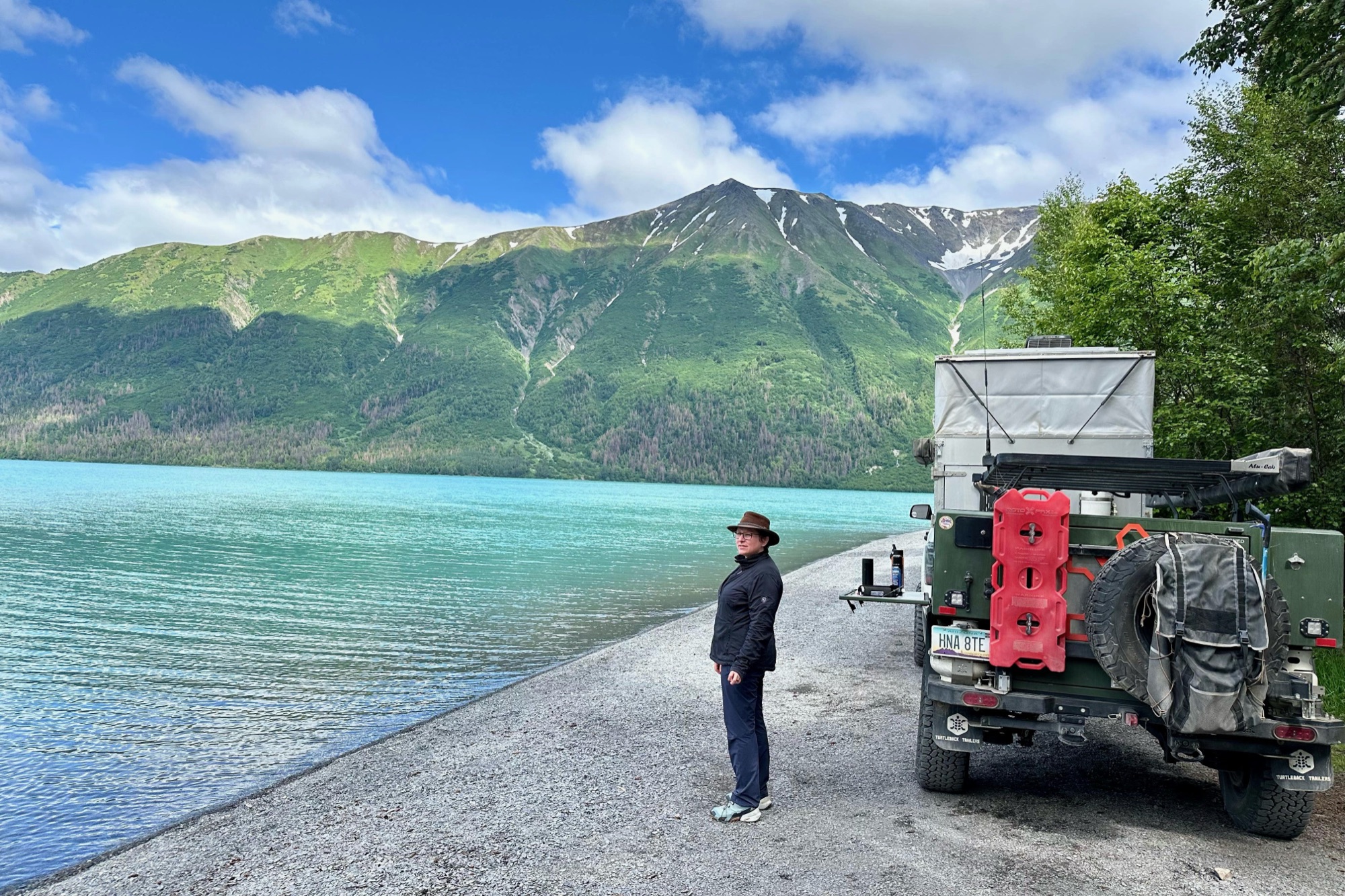 Keith standing beside the trailer at the edge of a turquoise Alaskan lake